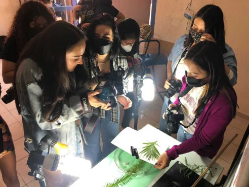 Alumnas con cámaras réflex alrededor de una mesa de fotografía de producto